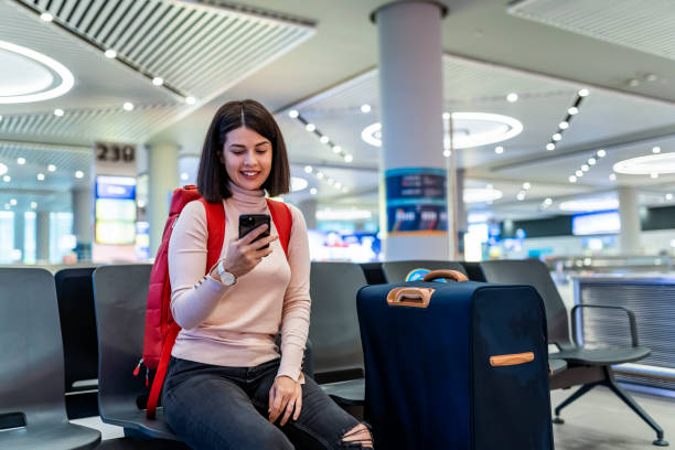 istock Young woman using mobile phone in airport waiting 1322290736