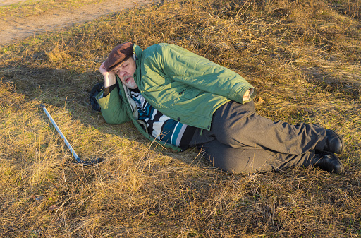 Caucasian senior hiker has short rest lying on the roadside at autumnal evening