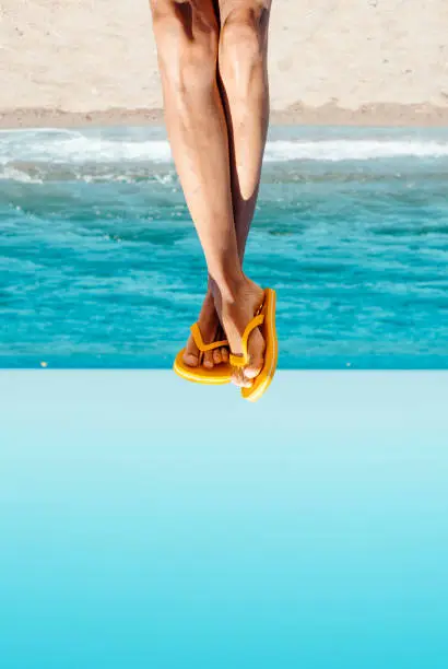 closeup of the legs of a young caucasian man on the beach wearing a pair of yellow flip-flops, upside-down,  with a blank space on the bottom