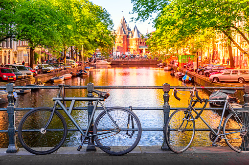 Old bicycles on the bridge in Amsterdam, Netherlands against a canal and old buildings during summer sunny day sunset. Amsterdam postcard iconic view.