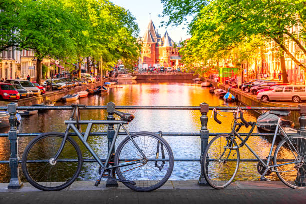 old bicycles on the bridge in amsterdam, netherlands against a canal and old buildings during summer sunny day sunset. amsterdam postcard iconic view. - amstel river amsterdam architecture bridge imagens e fotografias de stock