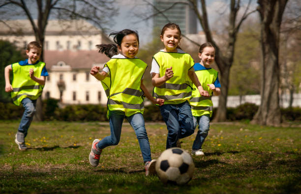 bambini piccoli che giocano a calcio all'aperto nel parco cittadino, imparando il concetto di educazione di gruppo. - attrezzatura per giochi allaperto foto e immagini stock