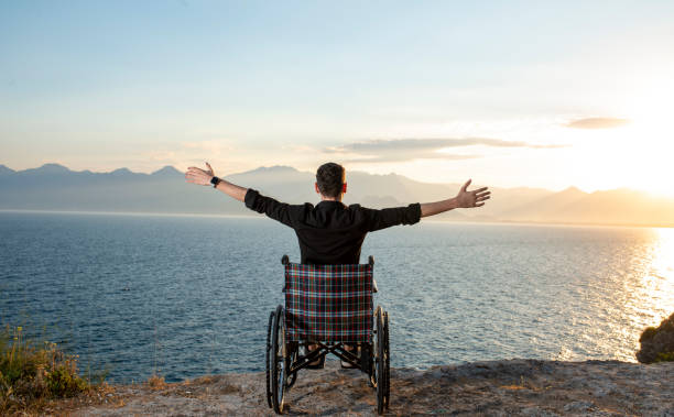 Silhouette of a disabled man in a wheelchair and his wife who is kissing. The concept of caring and supporting disabled people