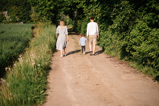 happy family mom, dad, son having fun and walking on country road, holding hand, rear view photo