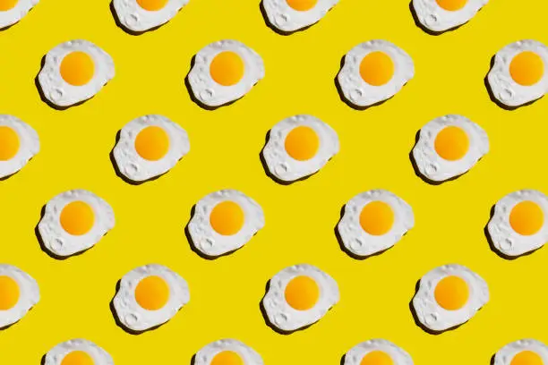 Fried egg pattern on bright yellow background. Abstract background food pattern.