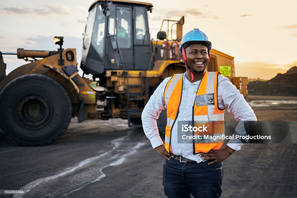 Foreman laughing A young Black African coal mine foreman looking off camera laughing wearing reflective bib and hard hat after a long day of work on site at the coal mine Occupation Stock Photo