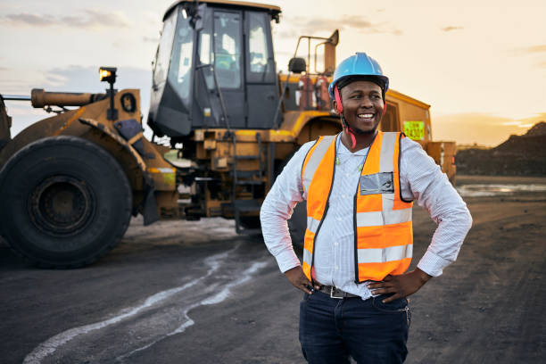 Foreman laughing A young Black African coal mine foreman looking off camera laughing wearing reflective bib and hard hat after a long day of work on site at the coal mine mining equipment stock pictures, royalty-free photos & images