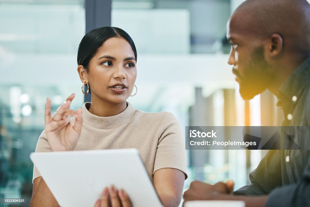 Shot of two work colleagues using a digital tablet during a business meeting at work You translate ideas well Discussion Stock Photo