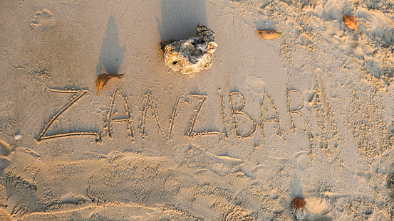 Word Zanzibar written on sand on the beach. Golden hour sunset time. Close up.