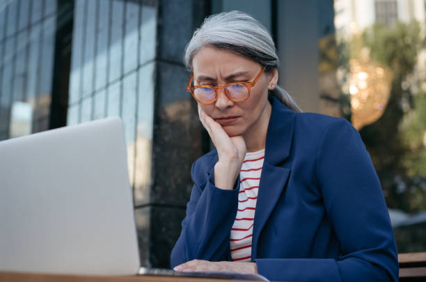 femme d’affaires asiatique fatiguée travaillant projet, en utilisant un ordinateur portable, la recherche d’informations, brainstorming. femme d’âge mûr frustrée assise sur le lieu de travail - typing busy business women photos et images de collection