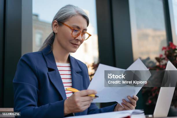 Mature Businesswoman Reading Contract Planning Project Brainstorming Portrait Of Attractive Asian Secretary Reading Working With Documents Sitting At Workplace Stock Photo - Download Image Now