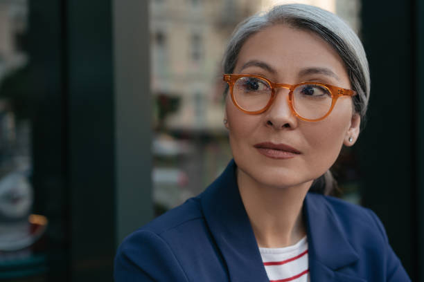 porträt einer nachdenklichen, reifen geschäftsfrau, die wegschaut und startup plant. schöne asiatische frau trägt stilvolle brille im freien stehen, fokus auf gesicht - women serious mature adult business stock-fotos und bilder