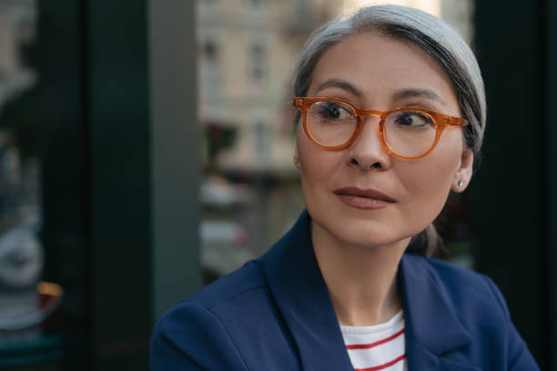 Portrait of pensive mature businesswoman looking away, planning start up. Beautiful asian woman wearing stylish eyeglasses standing outdoors, focus on face Close up portrait of pensive mature businesswoman looking away, planning start up. Beautiful asian woman wearing stylish eyeglasses standing outdoors, focus on face south east asian ethnicity stock pictures, royalty-free photos & images