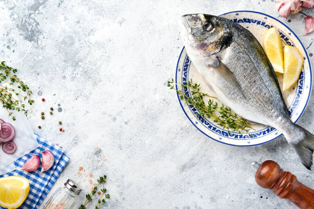 istock Raw dorado fresh fish or sea bream with ingredients for making lemon, thyme, garlic, cherry tomato and salt on light grey slate, stone or concrete background. Top view with copy space. 1322308249