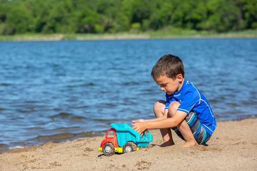 Close-up of a young boy (four years old) playing on the beach with a toy truck. Taken on a beautiful summer morning.
