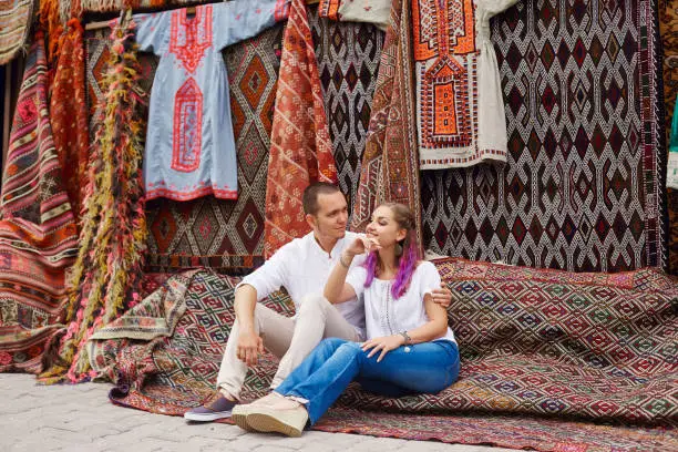 Photo of Couple in love buys a carpet and handmade textiles at an oriental market in Turkey. Hugs and cheerful happy faces of men and women