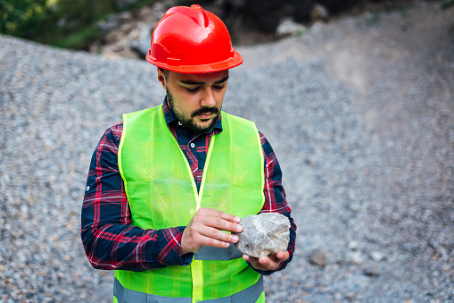 Young engineer with protective helmet examines a rock at quarry