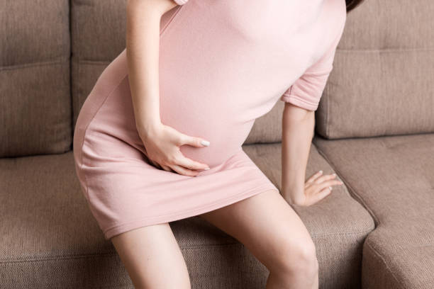 istock Pregnant Lady Having Massaging Lower belly Sitting On Sofa Indoor. Pregnancy Problems Concept. Maternity healthcare 1322316583