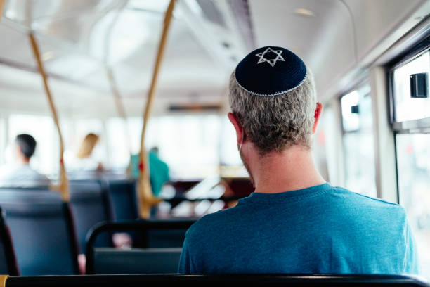 Jewish man wearing skull cap on bus in the city Color image depicting a mid adult Jewish man in his 30s wearing a traditional Jewish skull cap (with star of David design) on a bus in the city. Other passengers are defocused in the background. orthodox judaism photos stock pictures, royalty-free photos & images