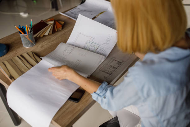 istock Blond female architect sitting at her desk and examining blueprints 1322318311