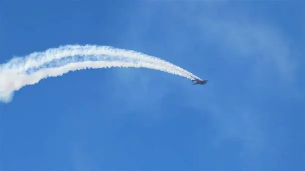 A Jet leaves white contrails arcing in blue sky at an air show. Copy Space.