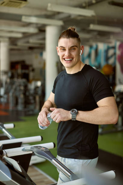 istock Happy athlete having water break and looking at camera while exercising on treadmill in a gym. 1322322397