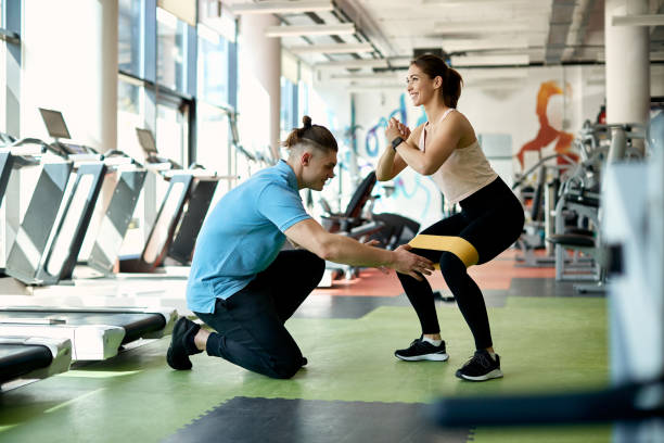 istock Happy sportswoman doing squats with resistance band on her legs while working out with fitness instructor in a gym. 1322322485