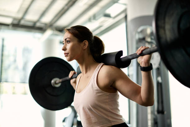 giovane donna atletica che si allena con il bilanciere durante l'allenamento con il peso in palestra. - weightlifting foto e immagini stock