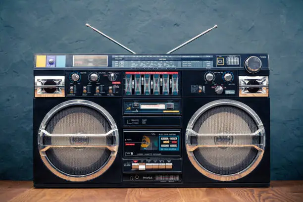 Photo of Retro boombox ghetto blaster outdated portable black radio receiver with cassette recorder from 80s front concrete wall background. Rap, Hip Hop, R&B music concept. Vintage old style filtered photo