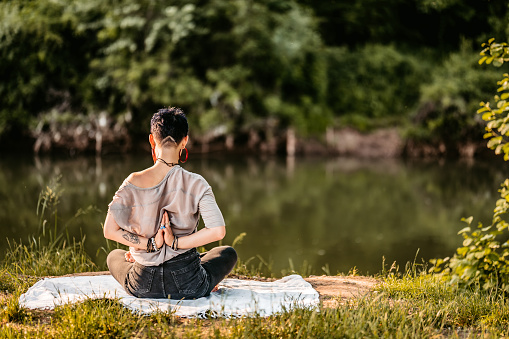 Portrait of young serene woman doing meditation by the river in nature.