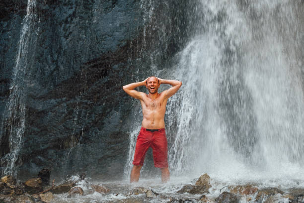 istock Middle-aged topless sincerely laughing man standing under the mountain river waterfall and enjoying the splashing Nature power. Fit people, trekking, and a natural beauty concept image. 1322327155