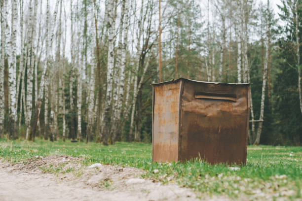 Garbage container in countryside in birch grove. Brown rusty trash can on the grass in forest