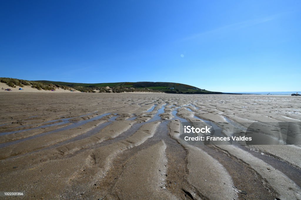 Ripples in the sand at Croyde Bay Devon. The photo is taken with a wide angle lens. The rippled sand fill the foreground and stretch to the distance. The sky is blue. The photo is taken at Croyde Bay which is a famous surfing beach in north Devon. It is situated in the south-west of the UK in an area often known as the West Country. It is a tourist destination. The photo was taken in April 2021. Beach Stock Photo