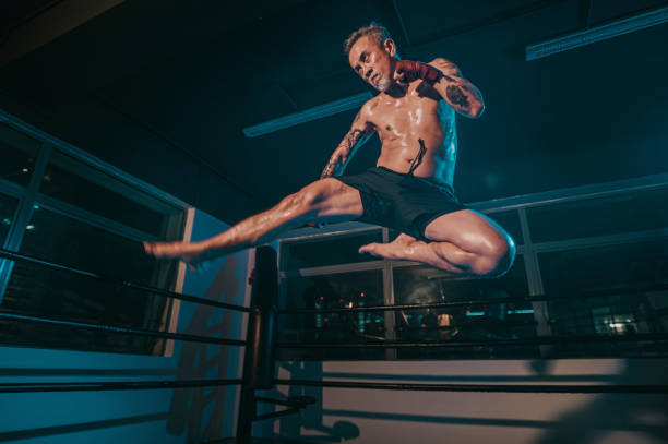 asiático chinês idoso salto chute em ringue de boxe de ginástica à noite - kickboxing muay thai exercising sport - fotografias e filmes do acervo