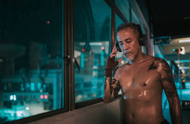 azjatycki chiński aktywny starszy bokser oczy zamknięte słuchanie muzyki ze słuchawkami obok okna na siłowni w nocy - harsh lighting audio zdjęcia i obrazy z banku zdjęć