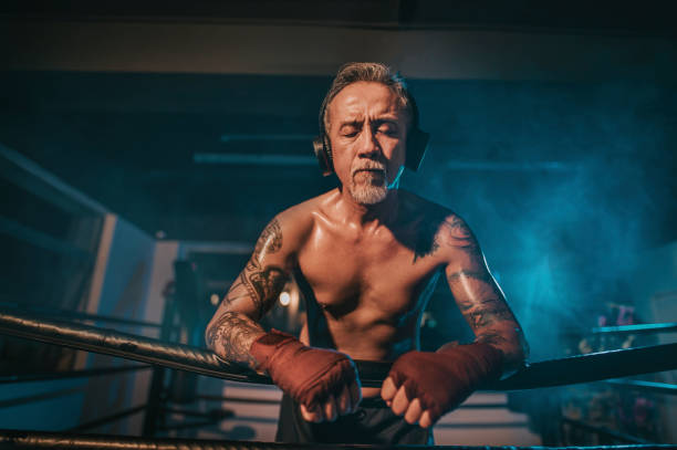 азиатский китайский активный старший боксер глаза человека закрыты опираясь на стороне боксерского ринга слушать музыку с наушниками при� - muay thai audio стоковые фото и изображения