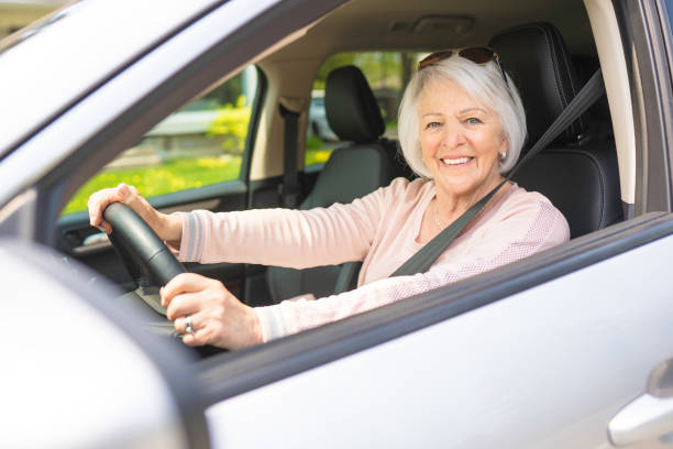 donna anziana felice e sorridente in auto bianca - driving senior adult car women foto e immagini stock