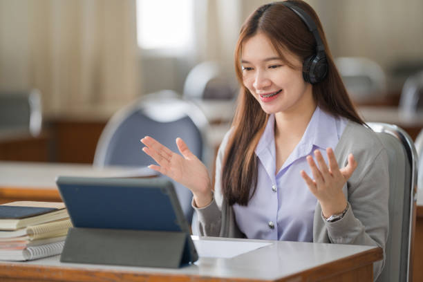 Young interactive happy Asian teenage girl university student studying and presenting her lesson online via video call on a digital tablet in the classroom alone herself. Education stock photo Young interactive happy Asian teenage girl university student studying and presenting her lesson online via video call on a digital tablet in the classroom alone herself. Education stock photo online tutors stock pictures, royalty-free photos & images