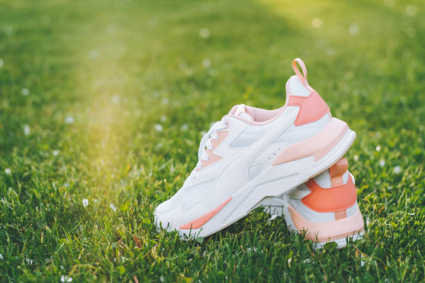 istock White women's sneakers with coral inserts standing on grass in rays of sunlight. Copy space 1322345073