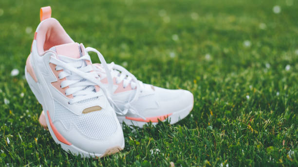 istock White women's sneakers with coral inserts standing on grass in rays of sunlight. Copy space. Banner 1322345428