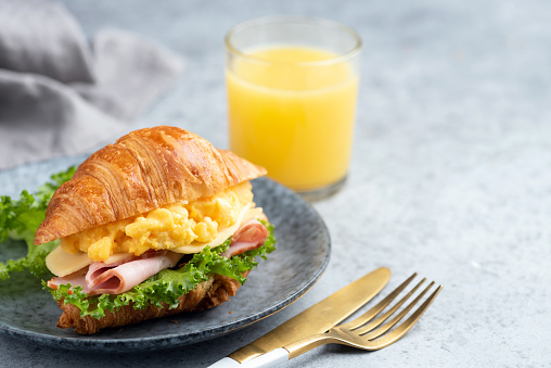 Breakfast croissant sandwich with ham and scrambled eggs on a plate. Continental breakfast food