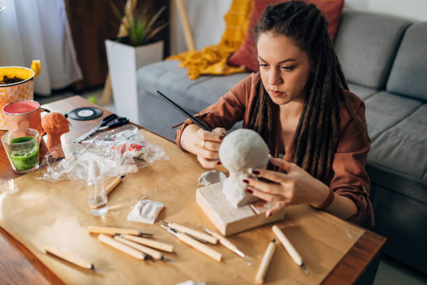 istock Alternative female artist, using a paintbrush while working on small details on her clay sculpture 1322355496