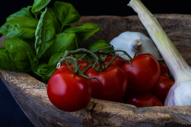 tomatoes, basil leaves and garlic in a old wooden bowl stock photo