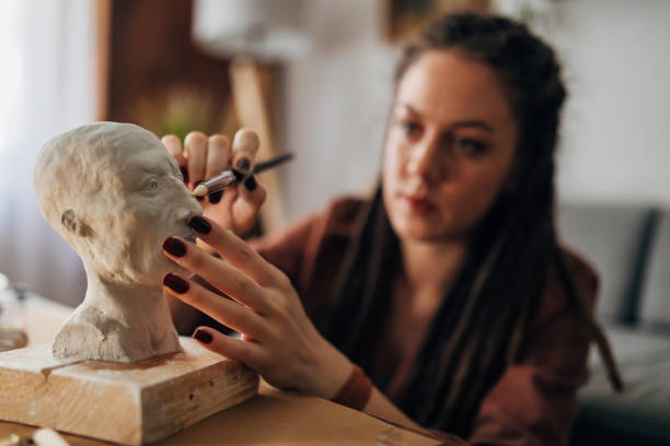 istock Alternative female sculptor, using a detailed brush while working on small details on her clay sculpture 1322355532