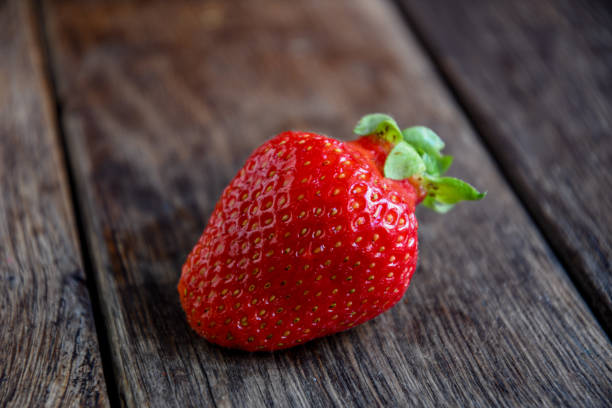 istock One strawberry on an old wooden table. 1322357069