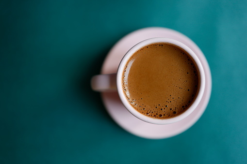 Istanbul, Turkey-June 7, 2021: Turkish Coffee with plenty of foam in a powder pink cup on a dark turquoise green background. There is empty space on the left side of the photo. Full frame, still life, sunlight. Shot with Canon EOS R5.
