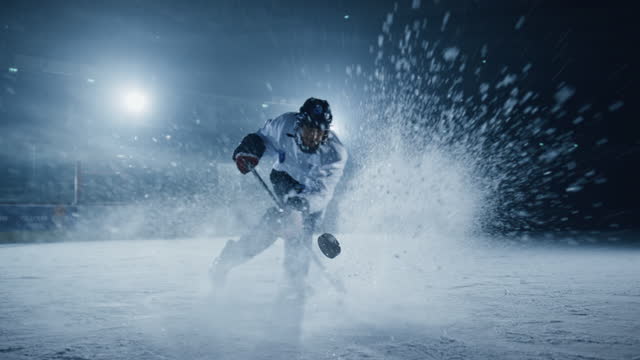 Ice Hockey Rink Arena: Professional Player Shooting, Hitting, Stricking the Puck with Hockey Sticks. Athlete Scoring a Goal. Dramatic Wide Shot, Cinematic Lighting, 3D Puck Flying in Slow Motion