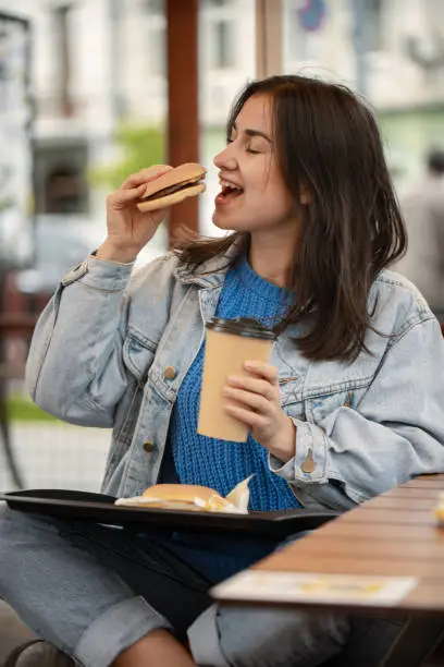 Photo of Street portrait of cheerful young woman eating fast food.