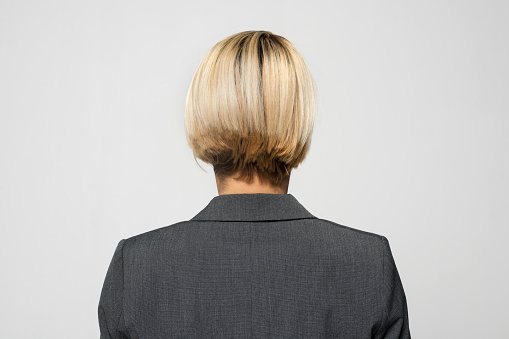 Rear view of mature businesswoman in grey blazer standing against grey background.