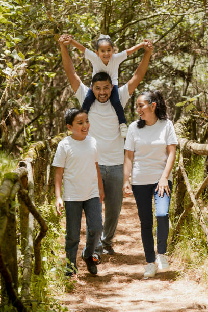 felice famiglia ispanica che cammina nel parco naturale - giovani genitori con i loro figli nel parco -famiglia latina - family summer portrait nature foto e immagini stock